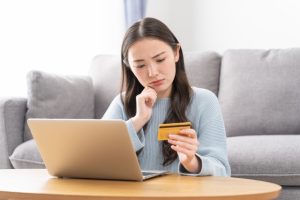 クレジットカードを持ち悩む女性の画像