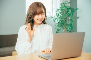 パソコンの前で挙手をする女性の画像